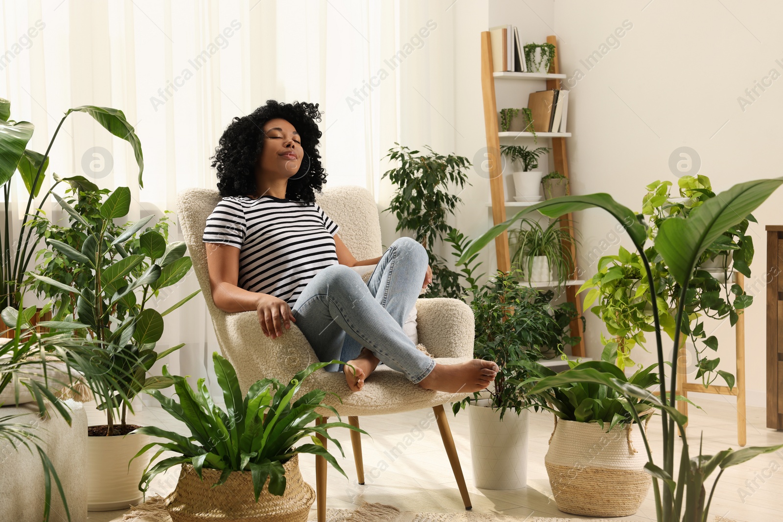 Photo of Woman relaxing in armchair surrounded by beautiful houseplants at home