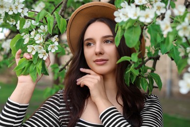 Beautiful woman in hat near blossoming tree on spring day