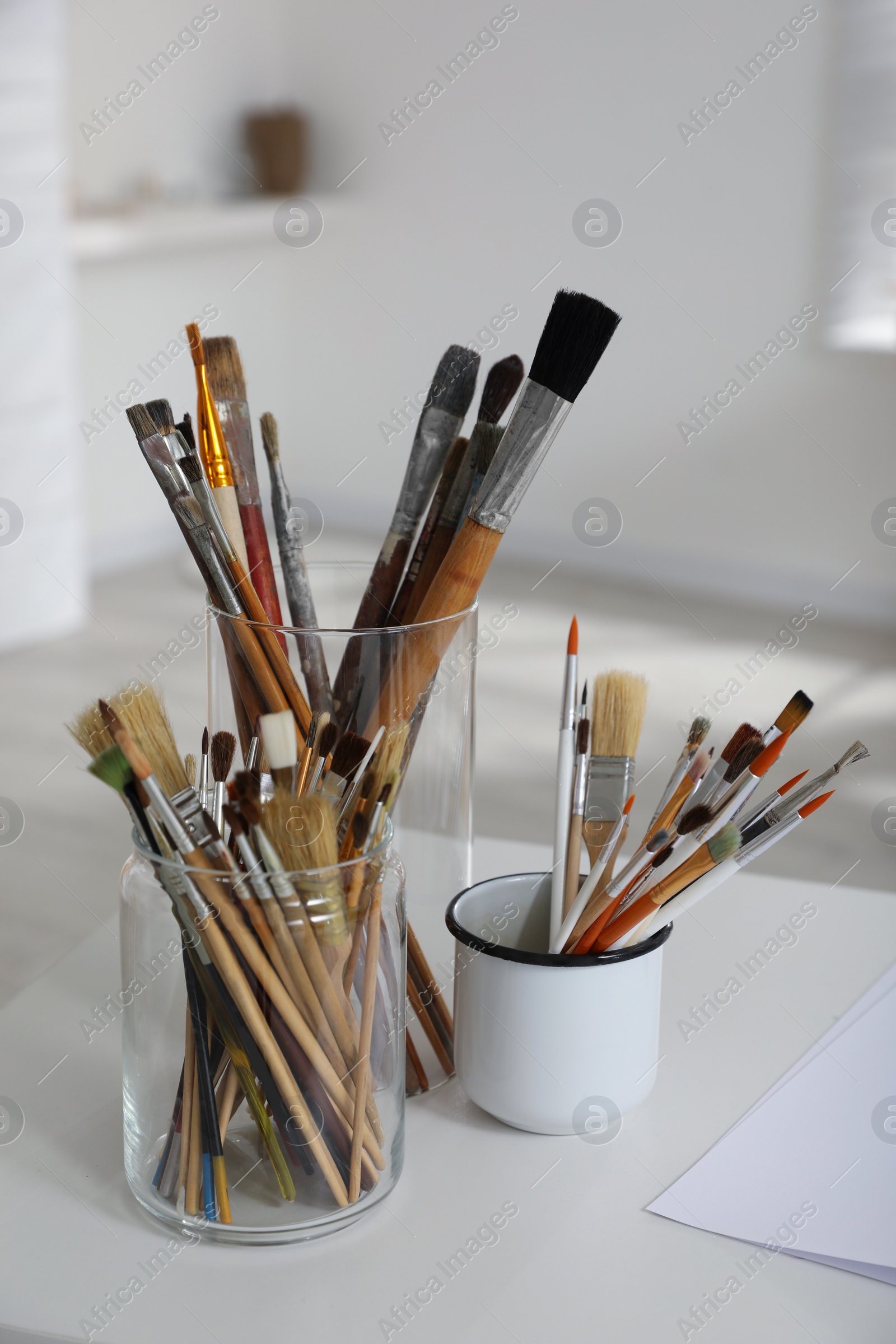 Photo of Holders with different paintbrushes on white table in studio. Artist's workplace