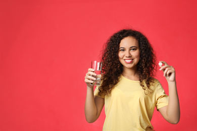 African-American woman with glass of water and vitamin pill on red background. Space for text
