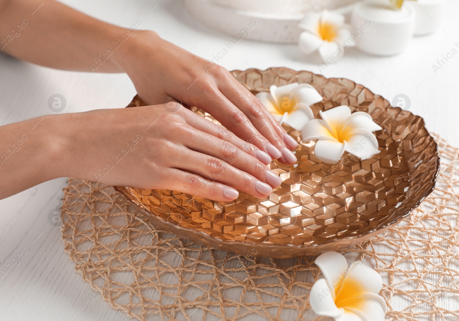 Photo of Woman soaking her hands in bowl with water and flowers on table, closeup. Spa treatment