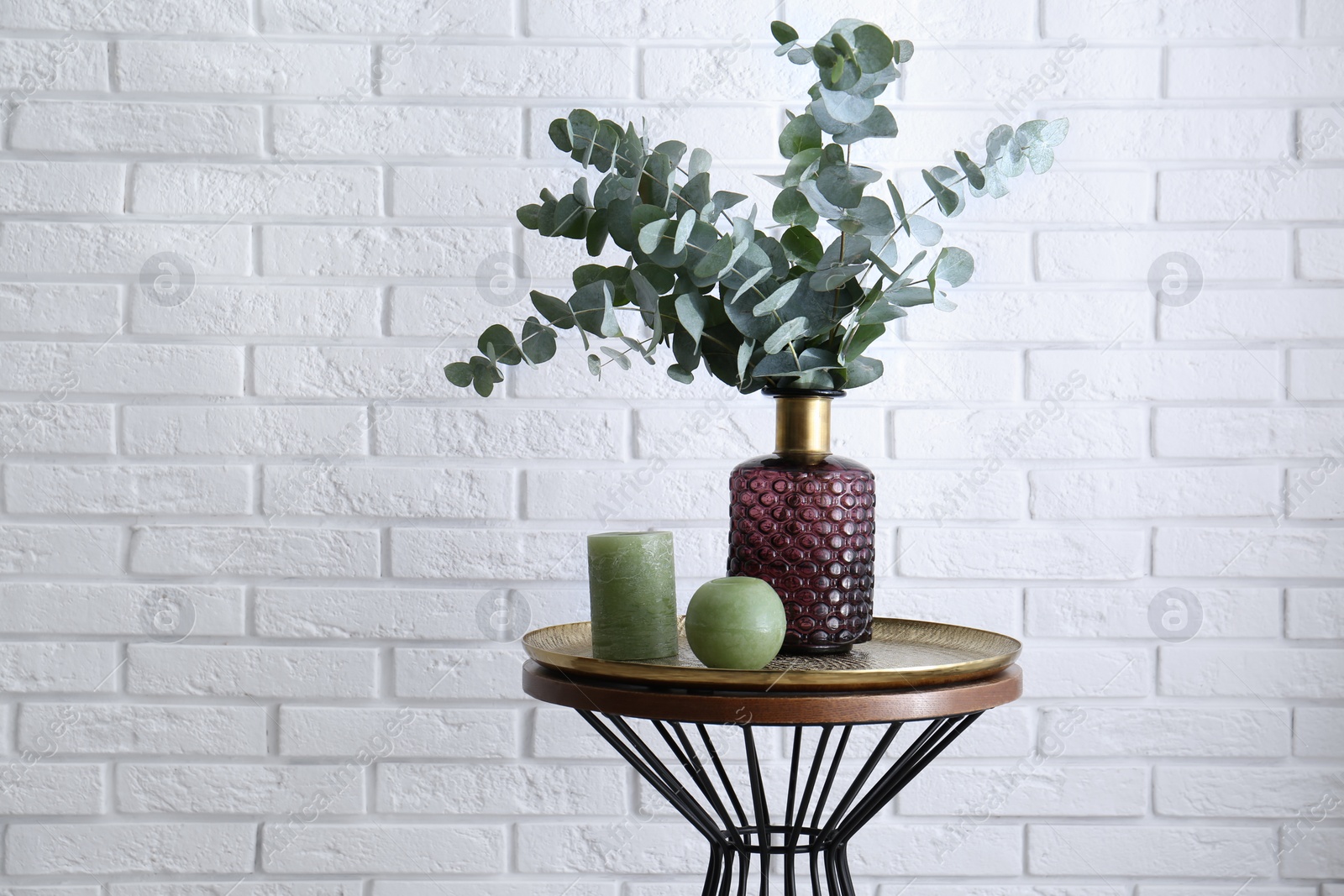 Photo of Eucalyptus branches and candles on table near white brick wall