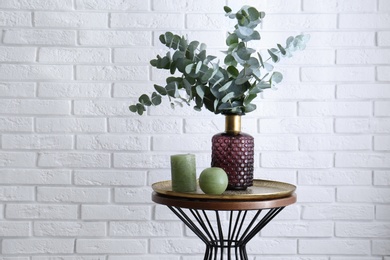 Eucalyptus branches and candles on table near white brick wall