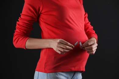 Young pregnant woman breaking cigarette on black background, closeup