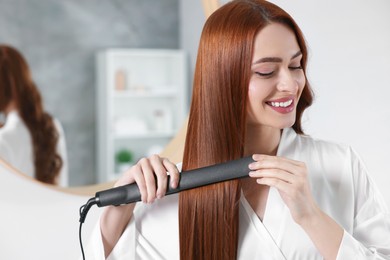 Photo of Beautiful woman using hair iron in room, space for text