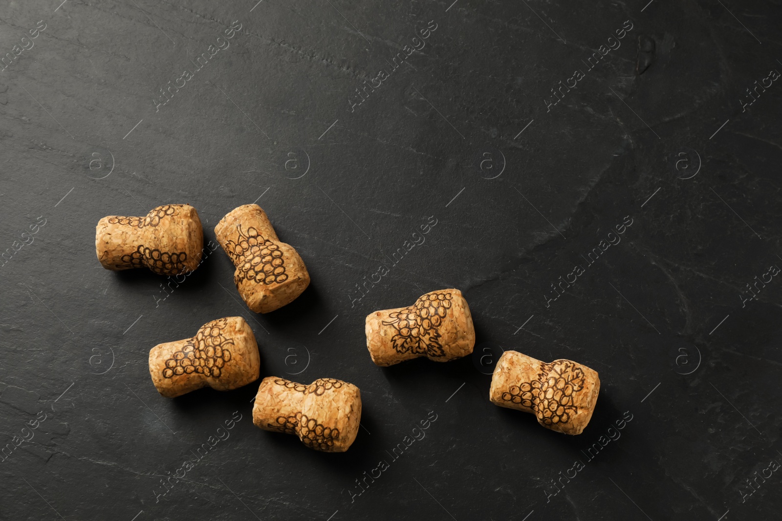 Photo of Sparkling wine corks with grape images on black table, flat lay. Space for text