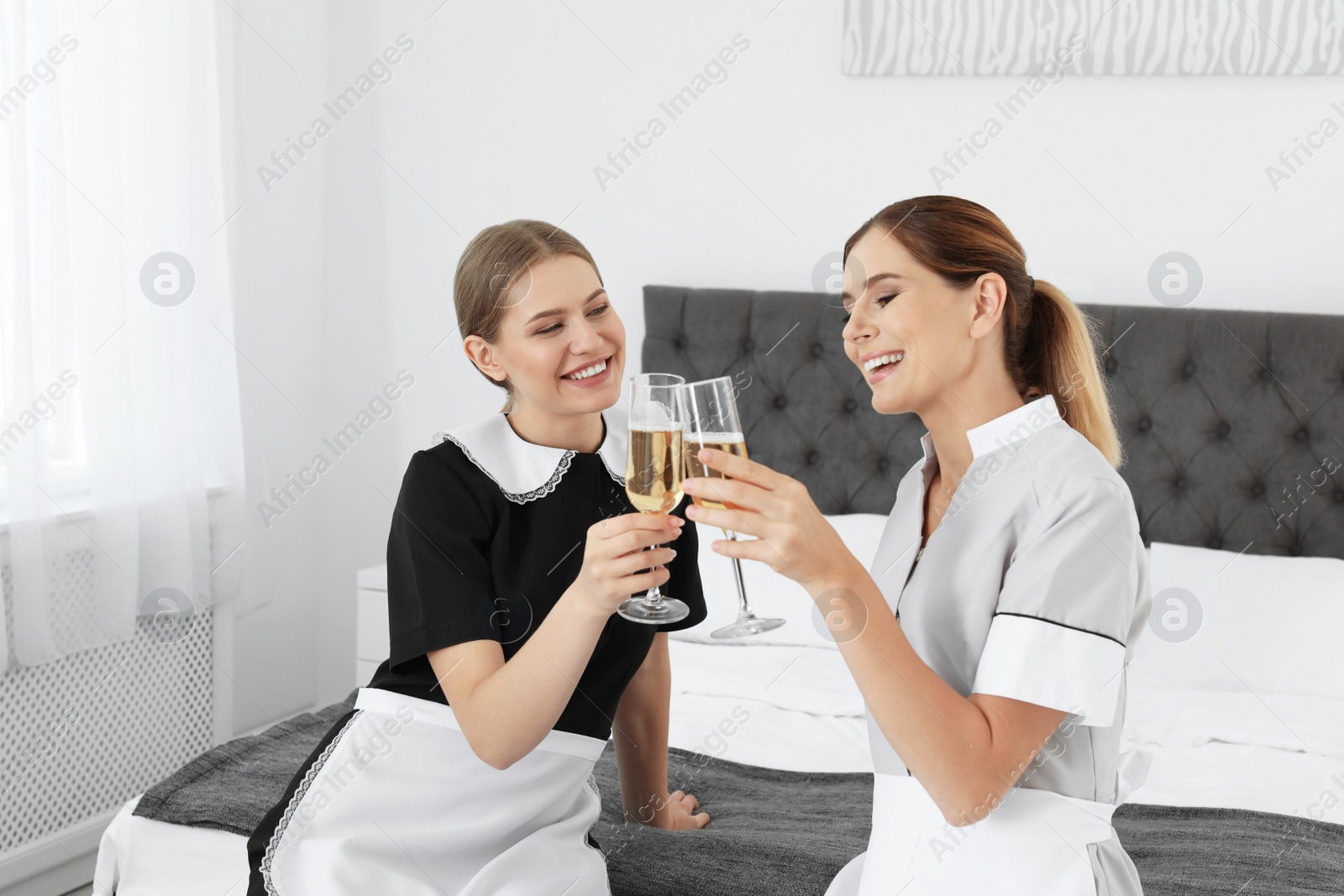 Photo of Happy young chambermaids drinking champagne in bedroom