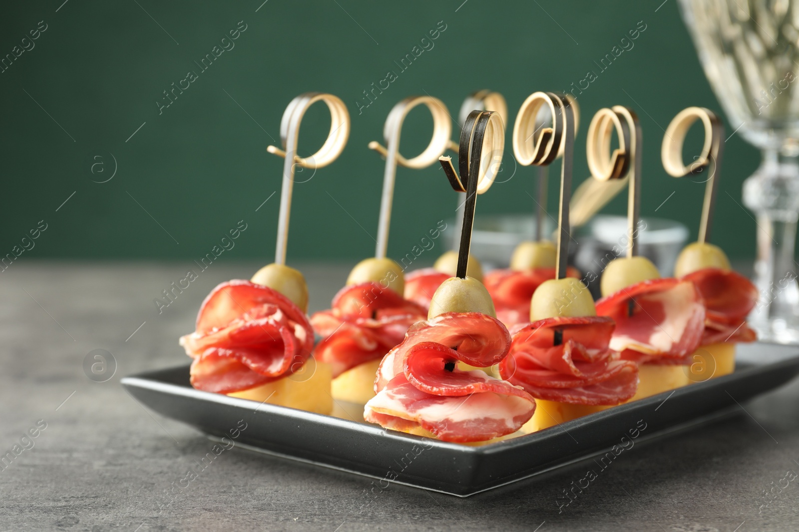 Photo of Tasty canapes with olives, prosciutto and cheese on grey table, closeup