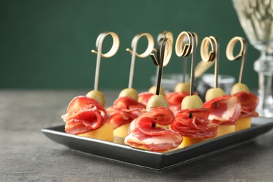 Tasty canapes with olives, prosciutto and cheese on grey table, closeup