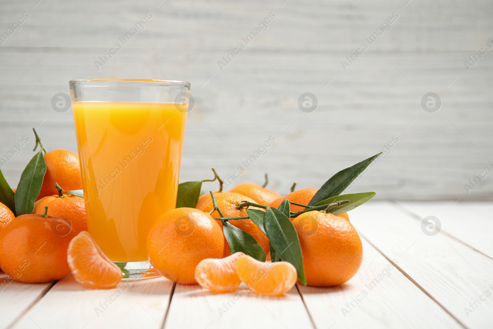 Photo of Glass of fresh tangerine juice and fruits on white wooden table