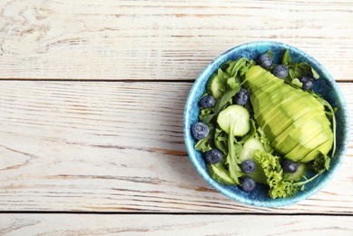 Delicious avocado salad with blueberries in bowl on white wooden table, top view. Space for text