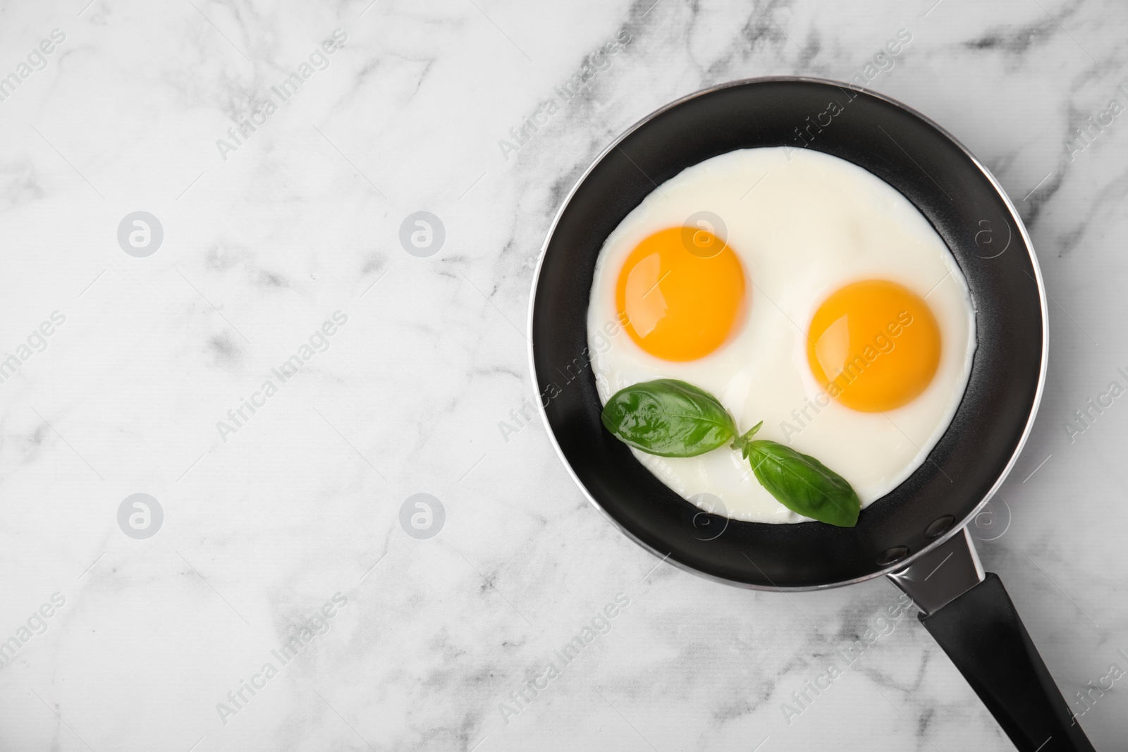 Photo of Tasty fried eggs with basil in pan on white marble table, top view. Space for text