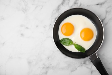 Tasty fried eggs with basil in pan on white marble table, top view. Space for text