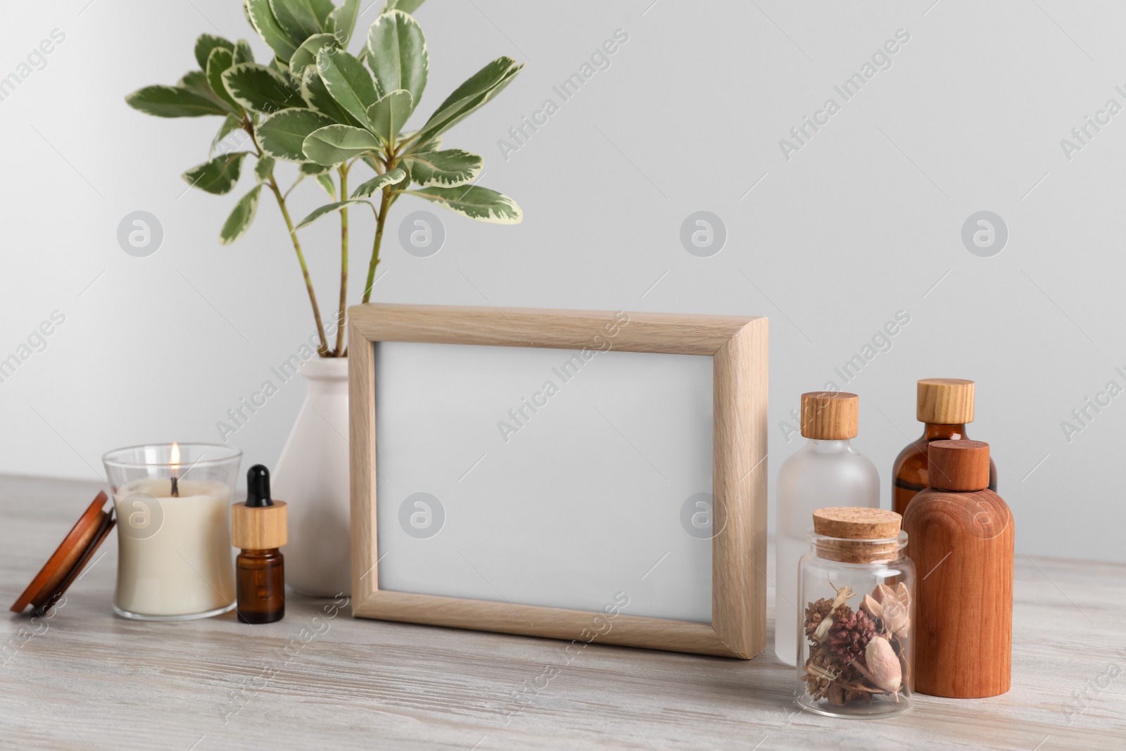 Photo of Blank photo frame, different bottles and decor elements on wooden table