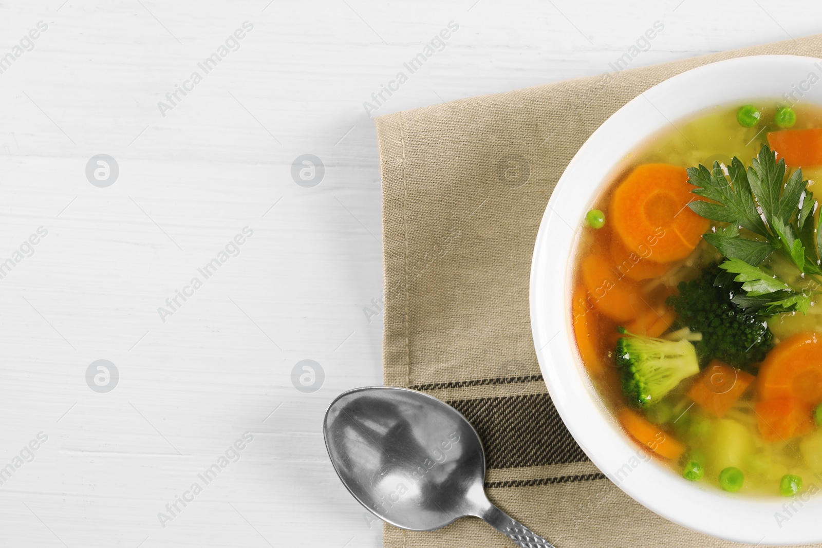 Photo of Delicious vegetable soup with noodles and spoon on white wooden table, top view. Space for text