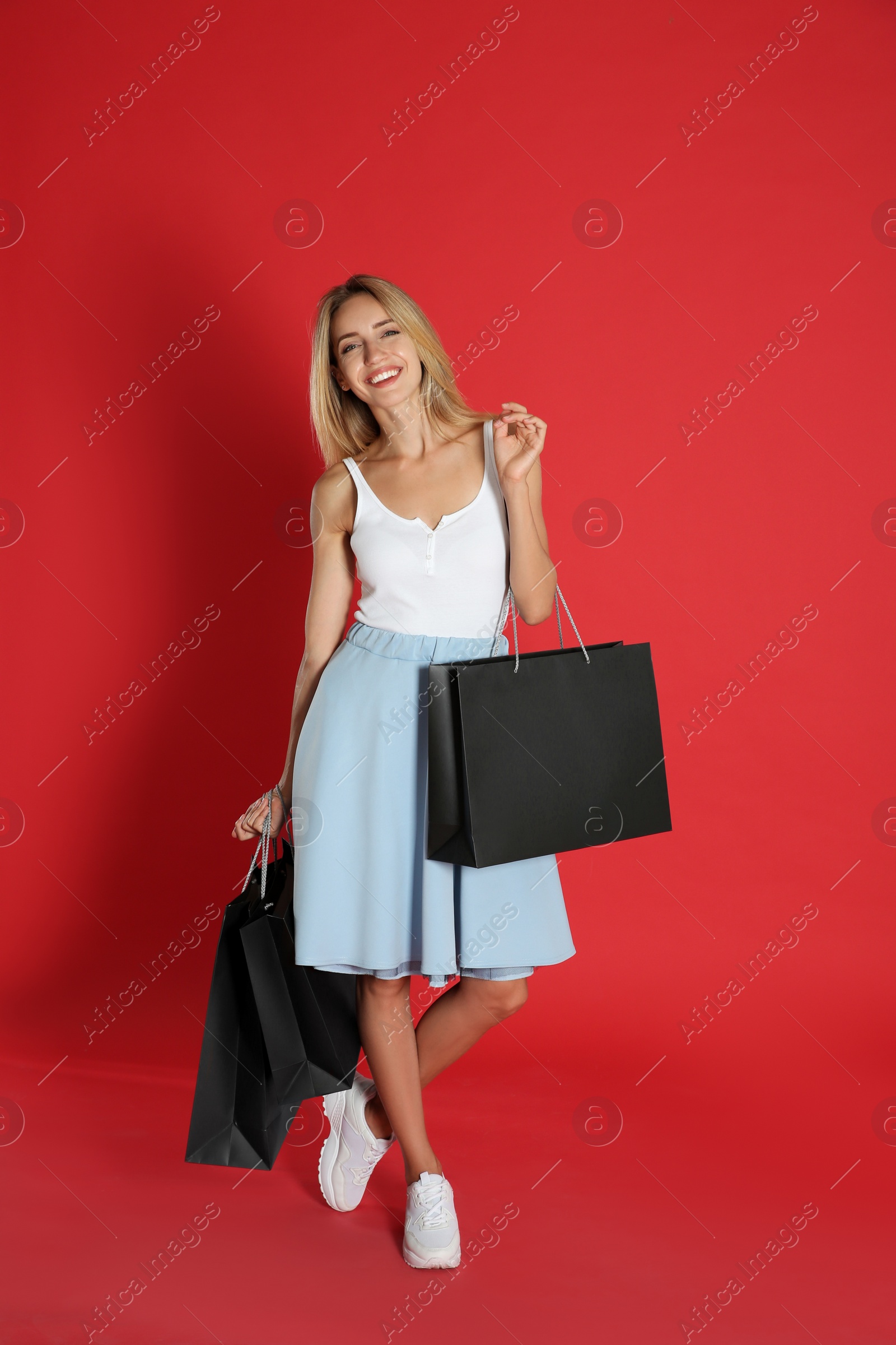 Photo of Happy young woman with shopping bags on red background. Black Friday Sale