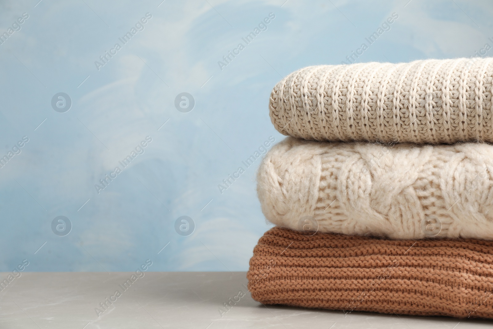 Photo of Stack of folded knitted sweaters on table. Space for text