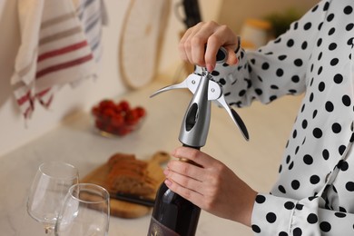 Photo of Romantic dinner. Woman opening wine bottle with corkscrew in kitchen, closeup