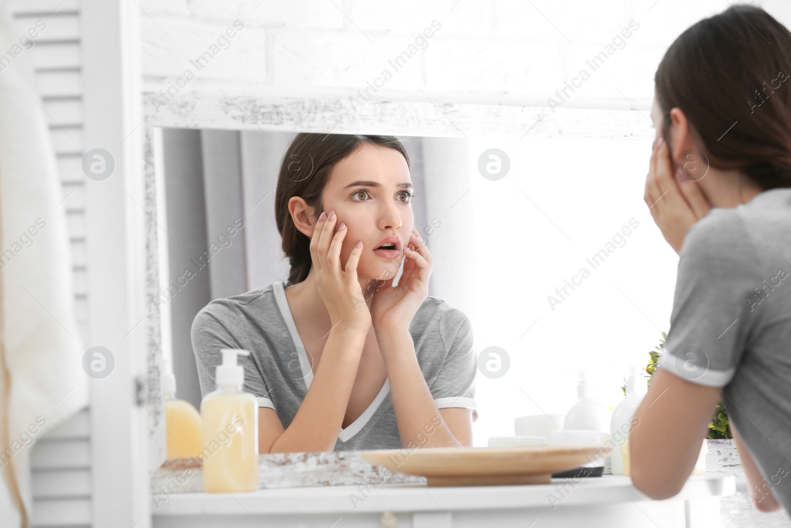 Photo of Teenage girl with acne problem looking in mirror indoors