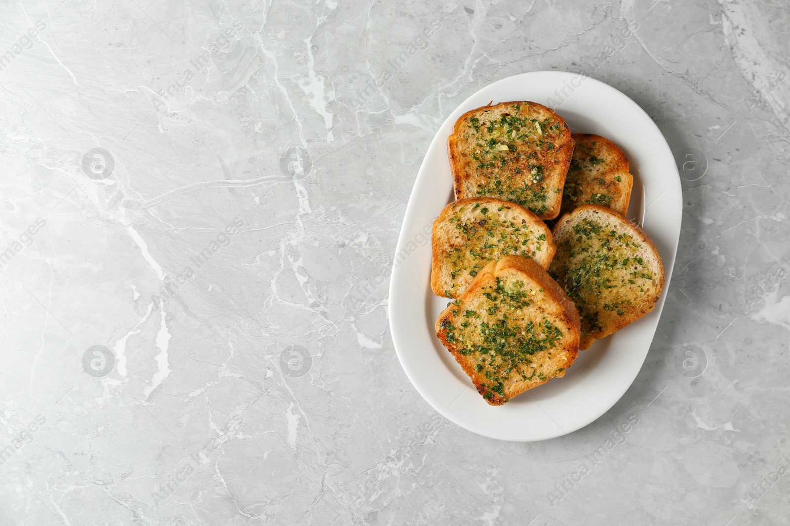 Photo of Slices of toasted bread with garlic and herbs on grey table, top view. Space for text