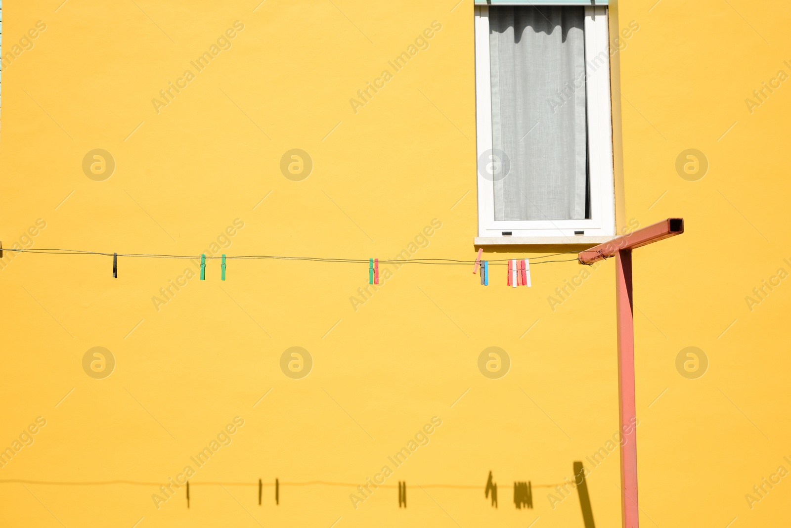 Photo of Many clothespins on rope near yellow house wall. Space for text