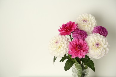 Photo of Bouquet of beautiful Dahlia flowers near white wall, space for text