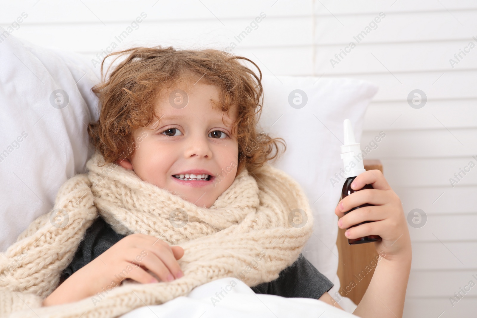Photo of Happy little boy with nasal spray on bed