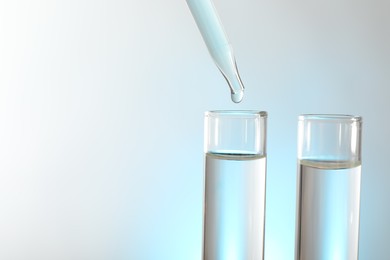 Photo of Dripping liquid from pipette into test tube on light background, closeup. Space for text