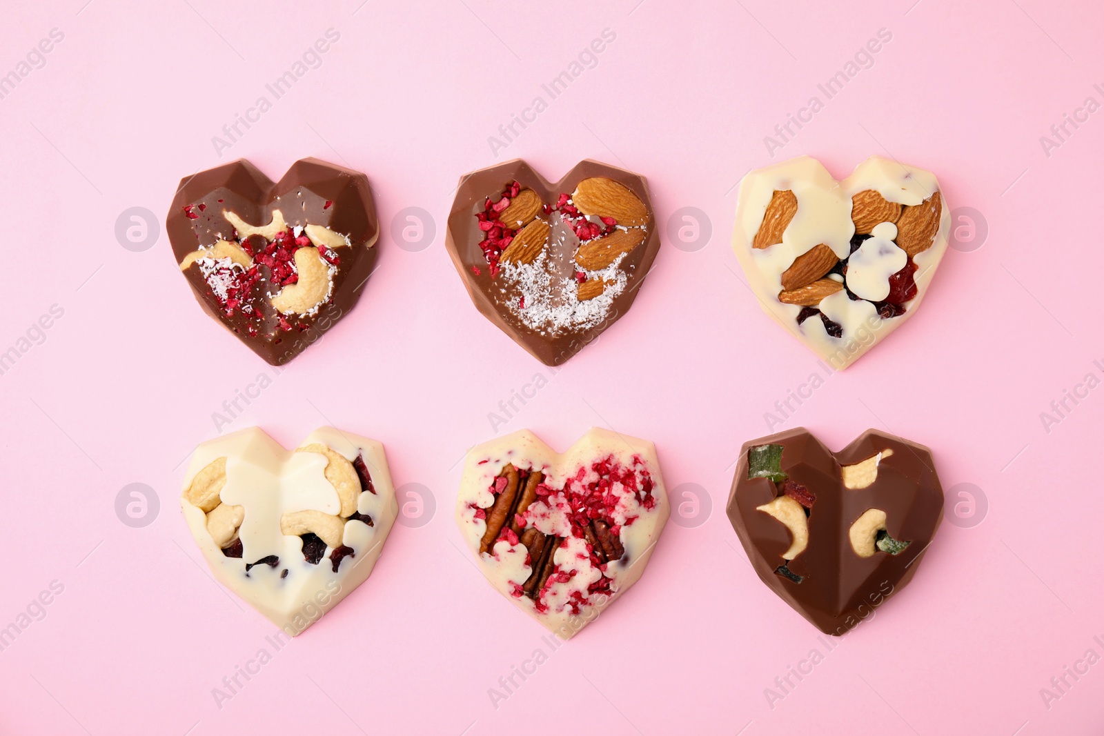 Photo of Tasty chocolate heart shaped candies with nuts on pink background, flat lay