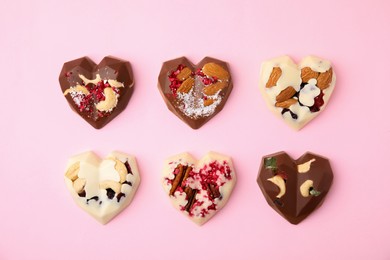 Photo of Tasty chocolate heart shaped candies with nuts on pink background, flat lay
