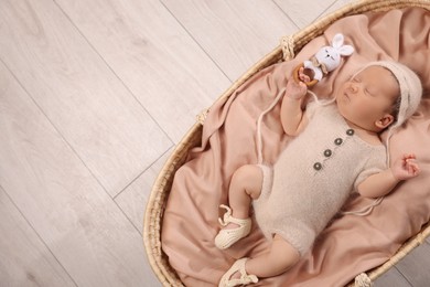 Photo of Cute newborn baby sleeping with rattle in wicker crib indoors, top view. Space for text