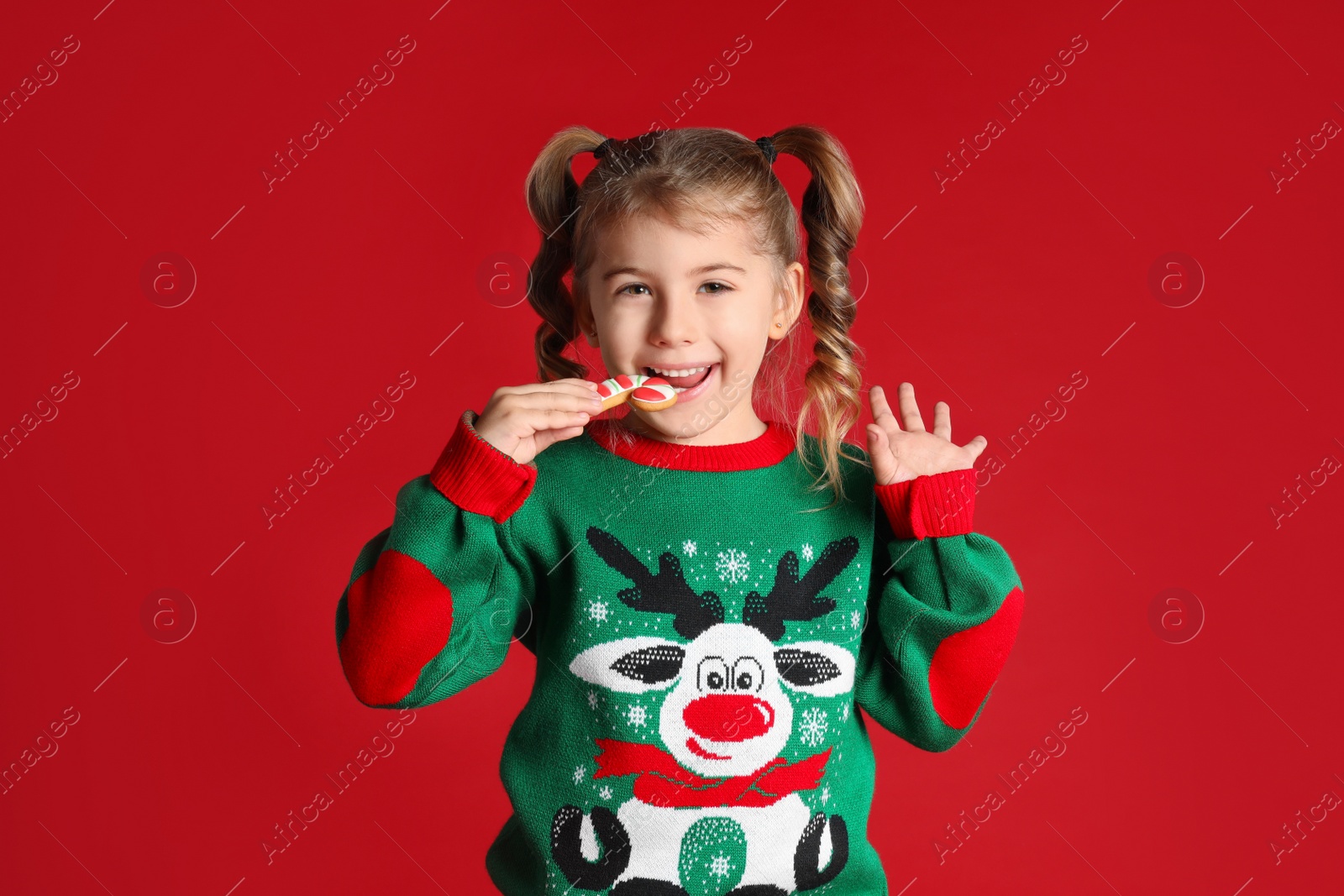 Photo of Cute little girl with Christmas gingerbread cookie on red background