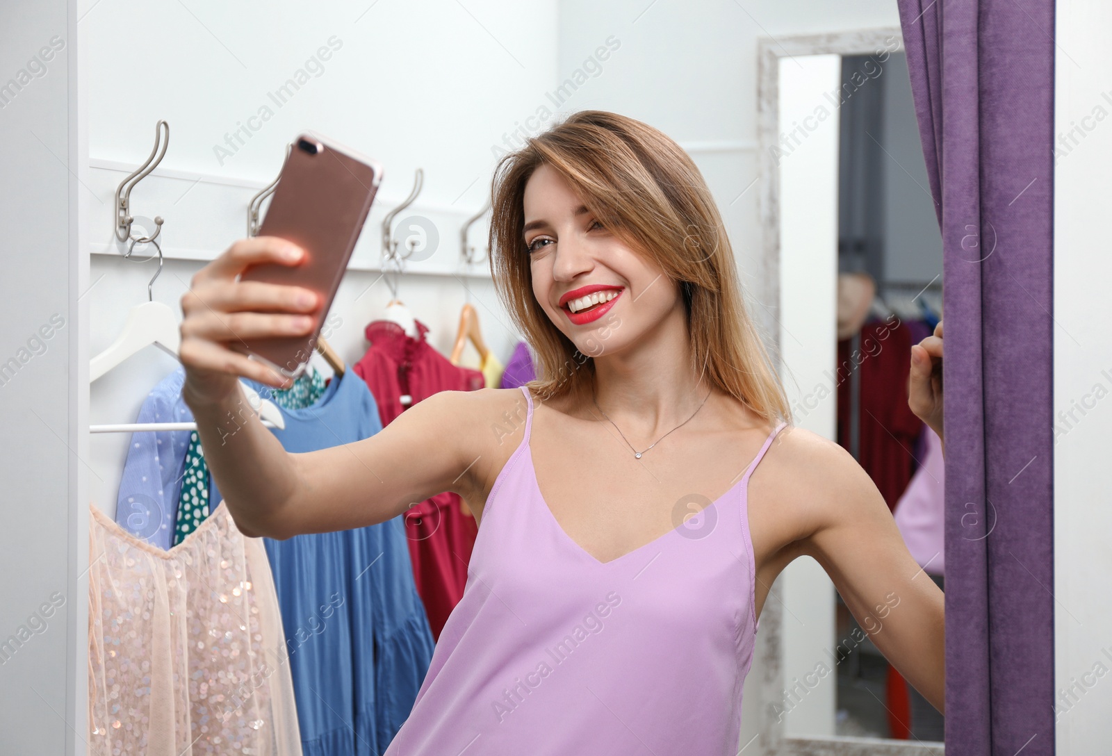 Photo of Young woman taking selfie in dressing room. Fashion store