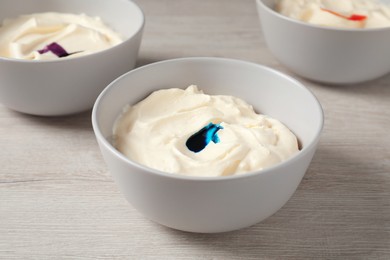 Bowls of different cream with food coloring on white wooden table, closeup