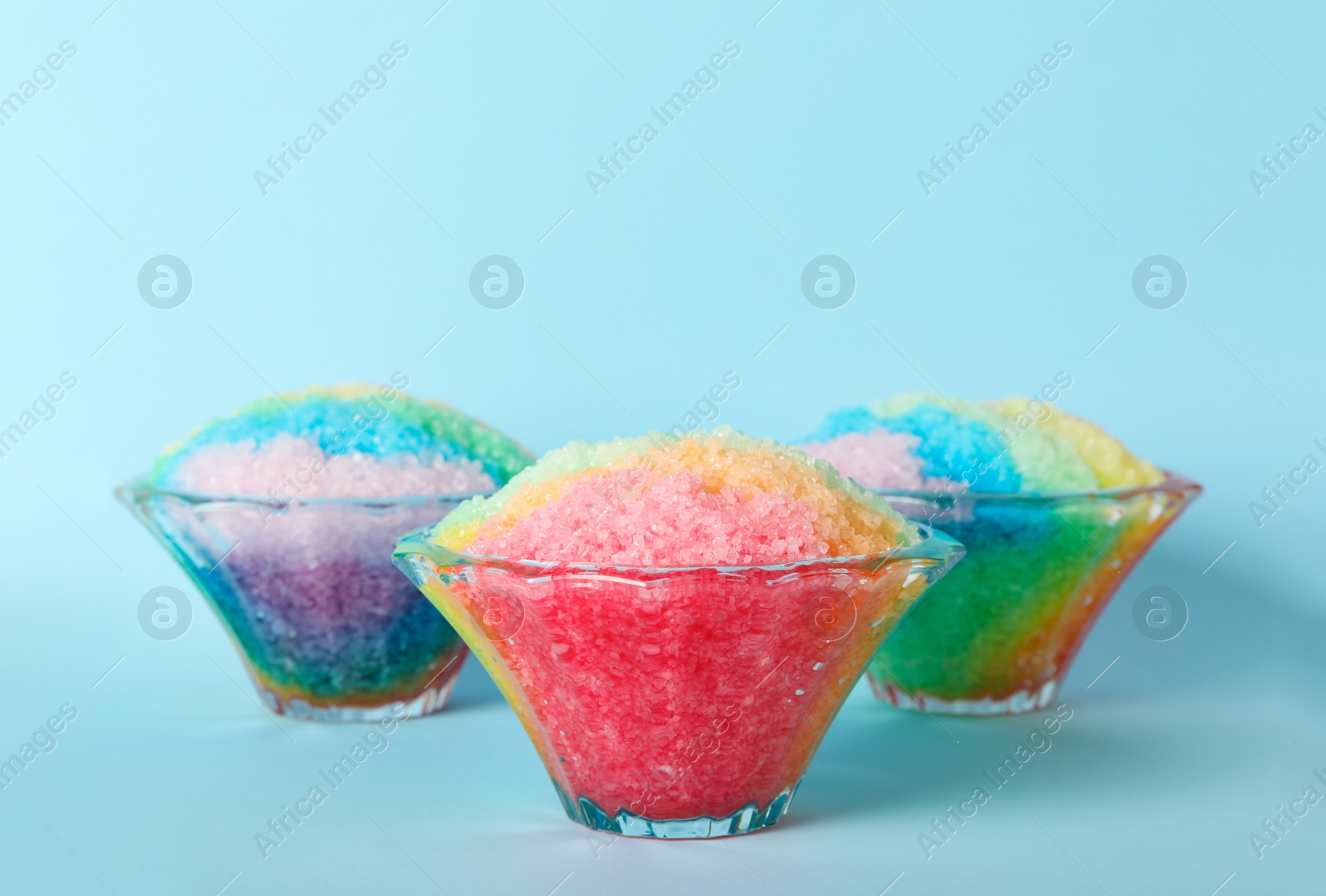 Photo of Rainbow shaving ice in glass dessert bowls on light blue background