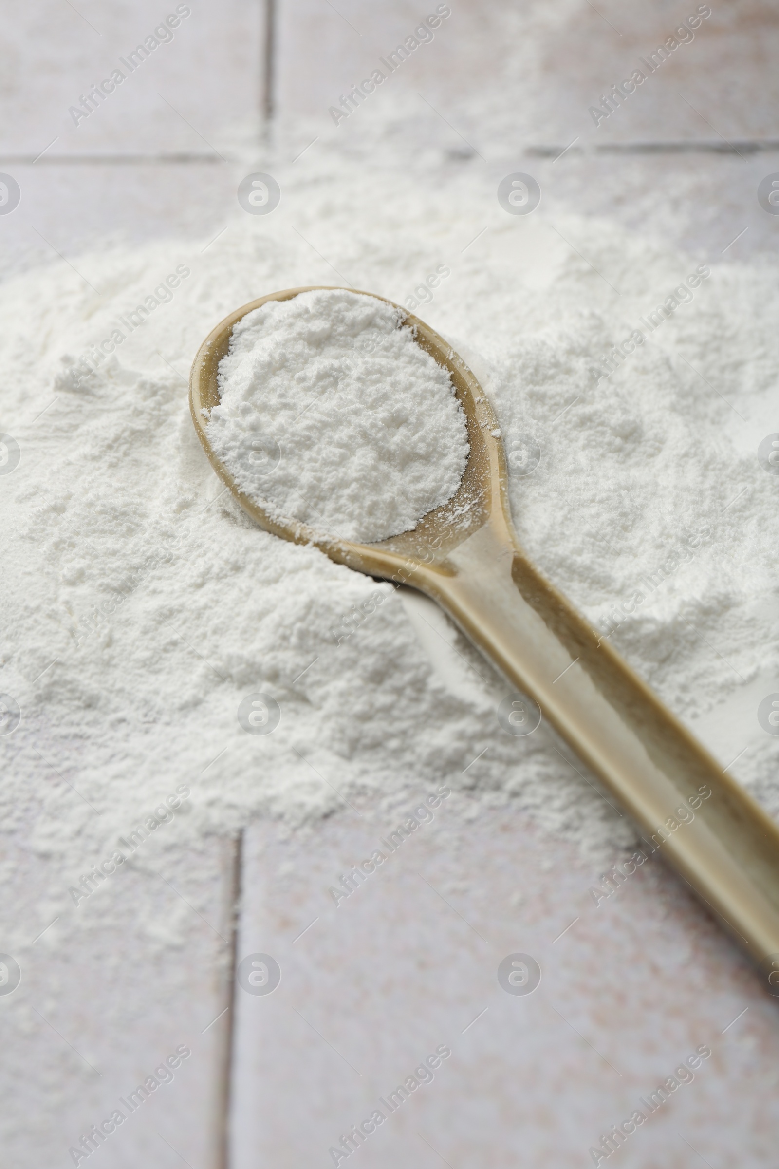 Photo of Pile of baking powder and spoon on light tiled table, closeup