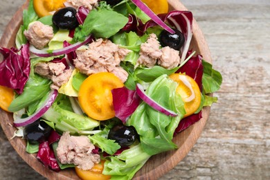 Photo of Bowl of delicious salad with canned tuna and vegetables on wooden table, top view