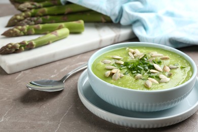 Photo of Delicious asparagus soup in bowl on grey marble table