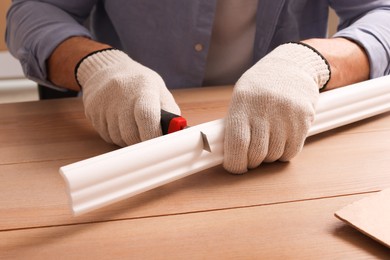 Man cutting foam crown molding with utility knife at wooden table, closeup