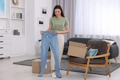 Photo of Happy woman with stylish light blue jeans at home. Online shopping