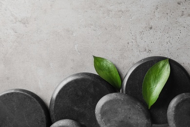 Flat lay composition with black spa stones and green leaves on color background. Space for text