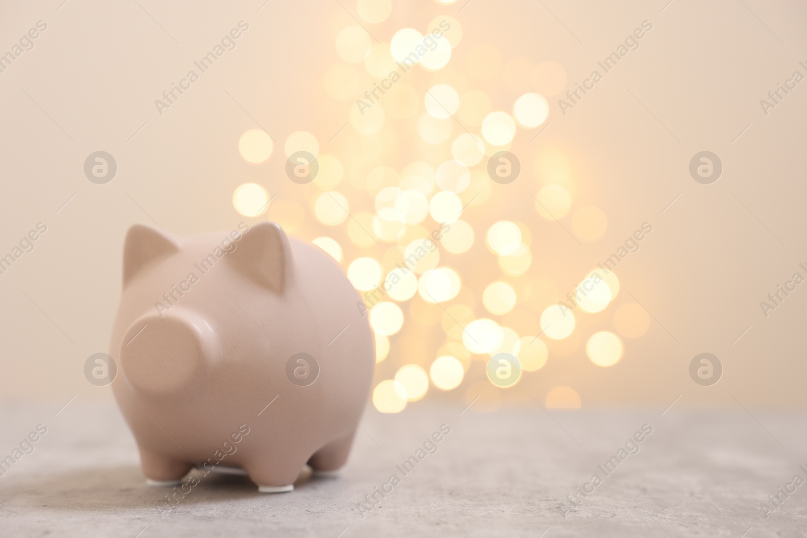 Photo of Piggy bank on grey table against blurred lights, space for text