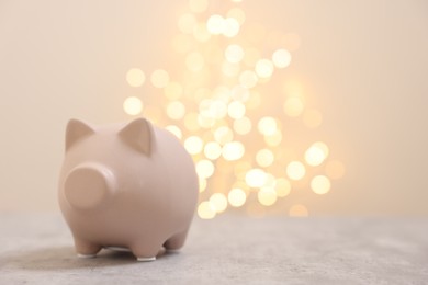 Photo of Piggy bank on grey table against blurred lights, space for text