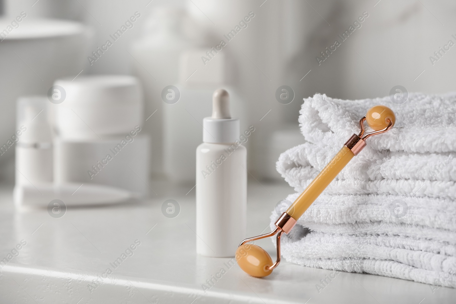 Photo of Natural face roller, towels and serum on counter in bathroom. Space for text