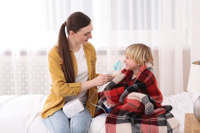 Photo of Mother helping her sick son with nebulizer inhalation in bedroom