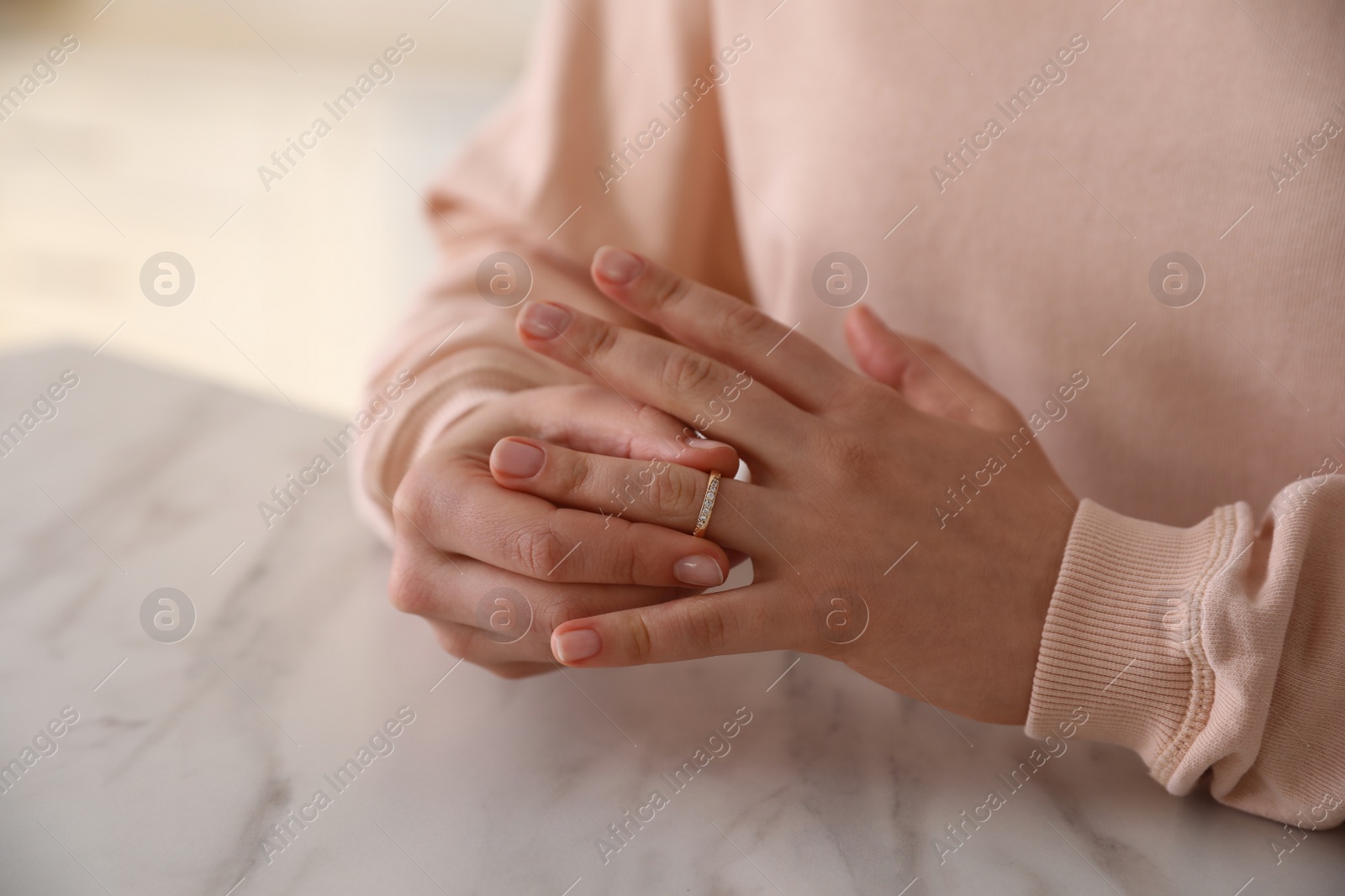 Photo of Woman taking off wedding ring at table indoors, closeup. Divorce concept