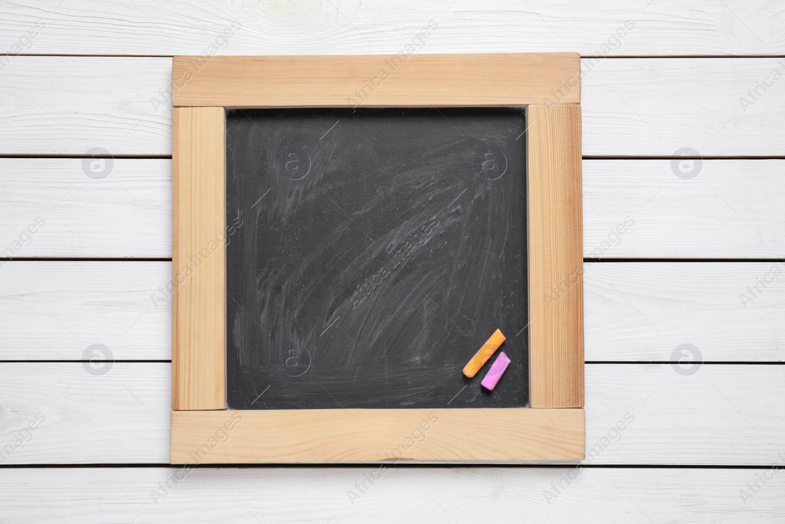Photo of Blackboard with pieces of color chalk on white wooden background, top view. Space for text