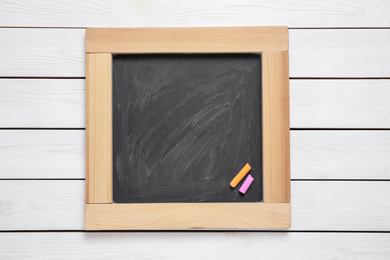 Photo of Blackboard with pieces of color chalk on white wooden background, top view. Space for text