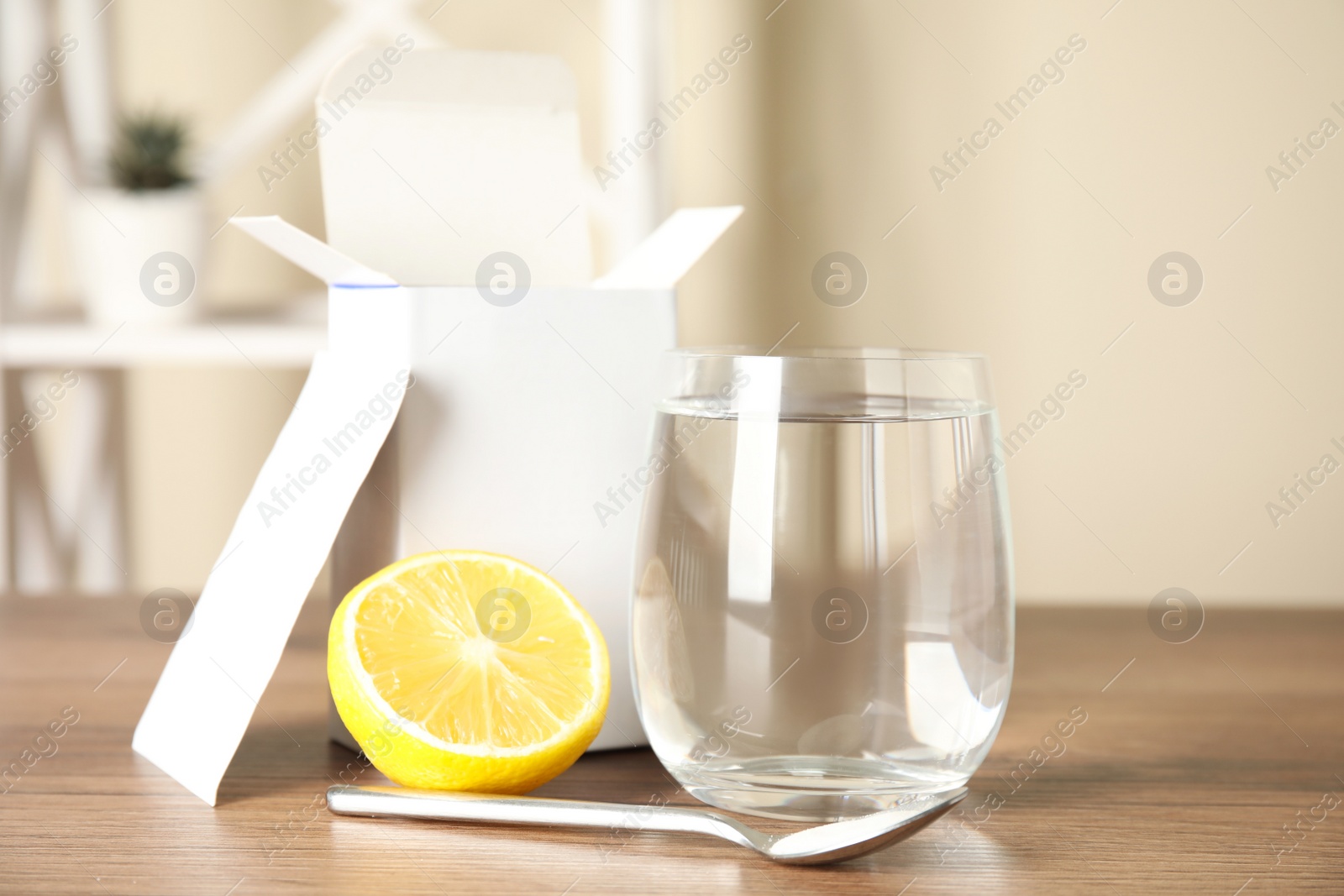 Photo of Medicine sachet, glass of water, spoon and lemon on wooden table