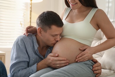 Photo of Man kissing his pregnant wife's belly at home